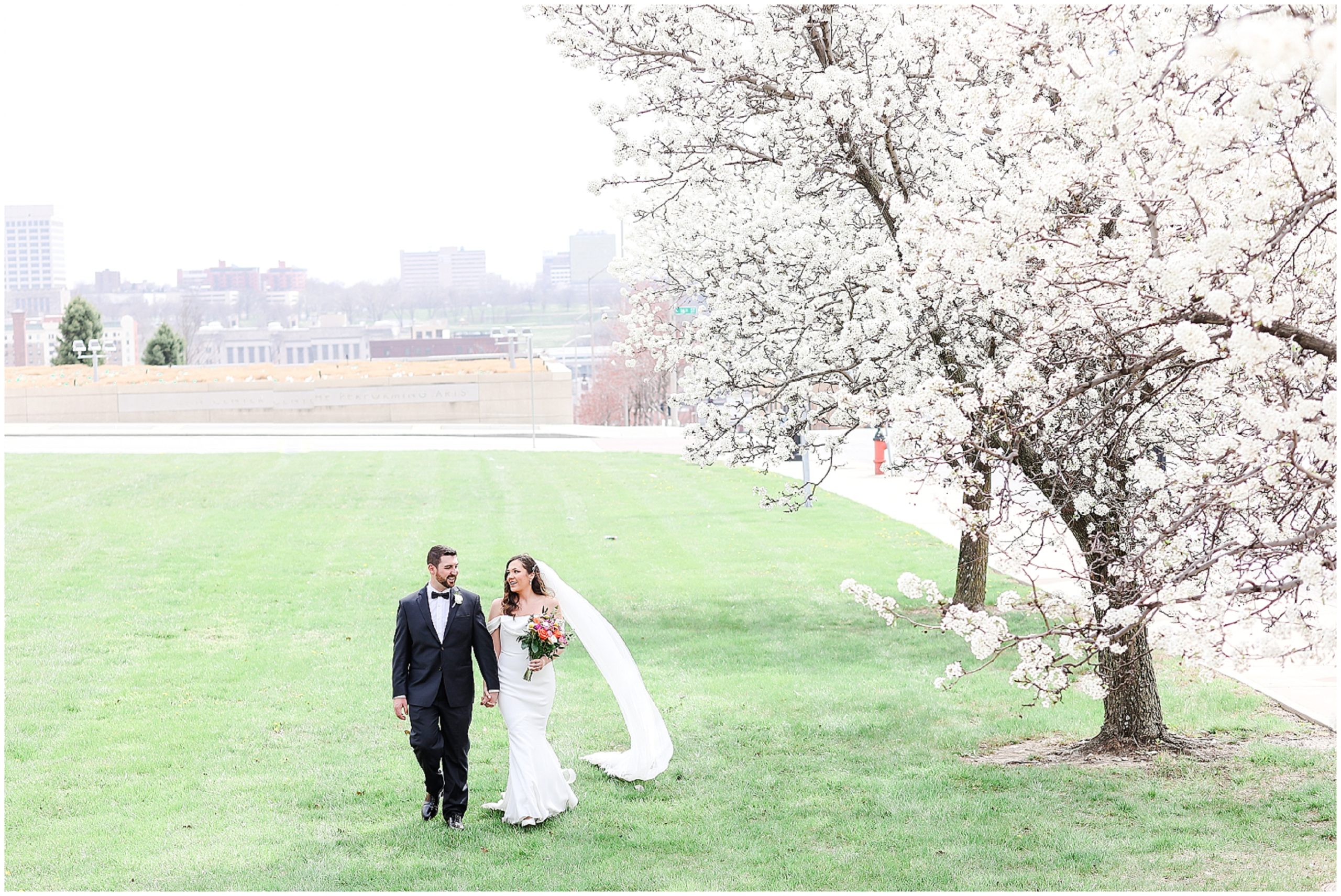 Beautiful wedding photos bride and groom walking in kansas city in front of kauffman center 